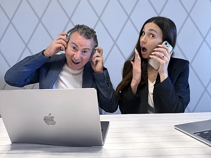 Dos integrantes del equipo de Velo en la oficina, con auriculares y teléfono, en un gesto divertido